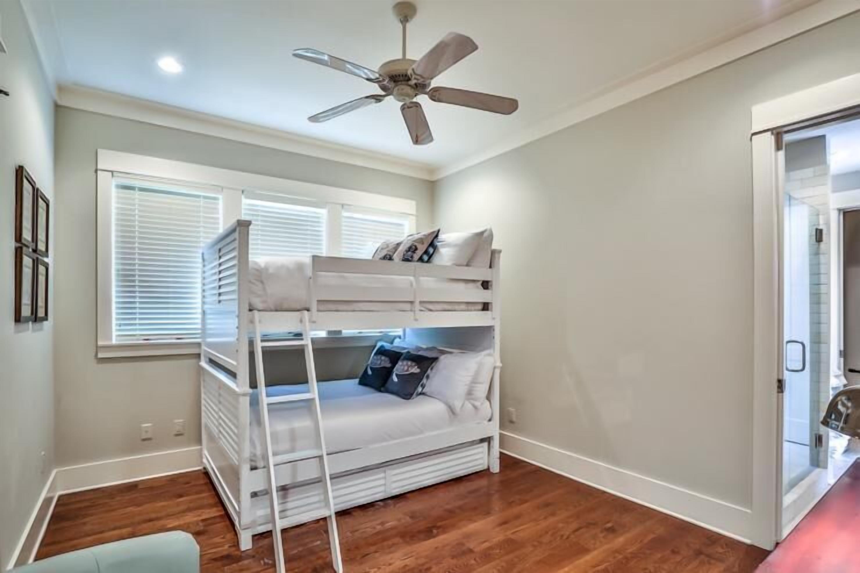A room with a bunk bed, a ceiling fan, and a window with blinds.