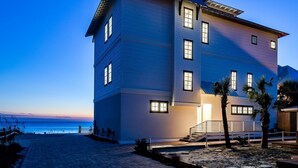Un hôtel à plusieurs étages avec vue sur la plage, doté d’une entrée imposante avec des marches et une rampe, et d’une porte bien visible portant l’inscription « Réception ».