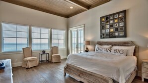 Une chambre spacieuse avec un grand lit, un plafond en bois et de nombreuses fenêtres équipées de stores.