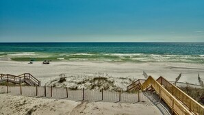 Une plage avec une promenade en bois menant à une zone sablonneuse, un ciel bleu dégagé et l’océan en arrière-plan.