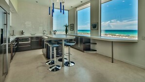 Une cuisine moderne dotée d’un grand îlot central, de tabourets de bar et offrant une vue sur la plage.