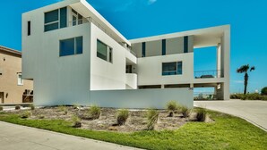 A modern, multi-story building with large windows and a flat roof, surrounded by a landscaped area with grass and small shrubs. - The White House of Holiday Isle 6 Bedroom Holiday Home by Five Star Properties (Destin)