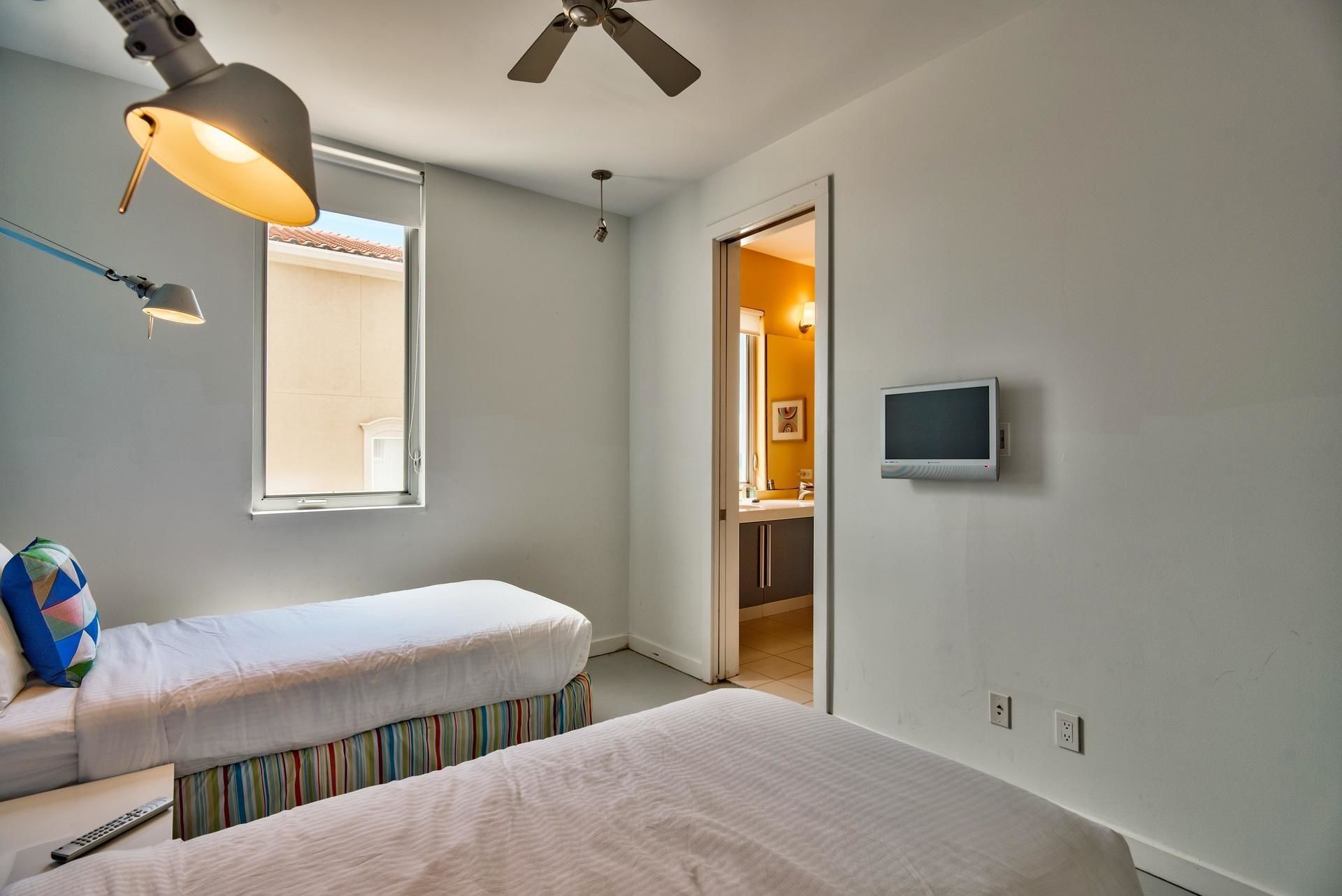 A bedroom with two beds, a ceiling fan, a TV, and a window.