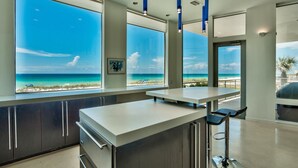 Une cuisine moderne dotée de grandes fenêtres donnant sur une plage, avec un coin bar et une vue sur l’océan.