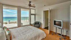 A bedroom with a bed, a TV on a cart, a chair, and a balcony with a view of the beach. - The White House of Holiday Isle 6 Bedroom Holiday Home by Five Star Properties (Destin)