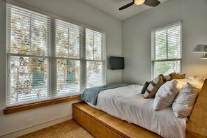 A bedroom with a bed, built-in bench, large windows, ceiling fan, and a wall-mounted TV. - The White House of Watercolor 4 Bedroom Holiday Home by Five Star Properties (Santa Rosa Beach)