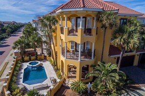 Un edificio amarillo de varios pisos con piscina, balcones y palmeras.