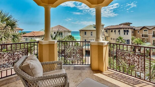 A balcony with wicker furniture, a view of the ocean, and a building with a tiled roof. - Tuscan Villa 5 Bedroom Holiday Home by Five Star Properties (Destin)