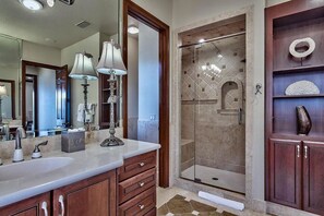 Un baño con un espejo grande, dos lavamanos, ducha con puerta de cristal y armarios de madera.
