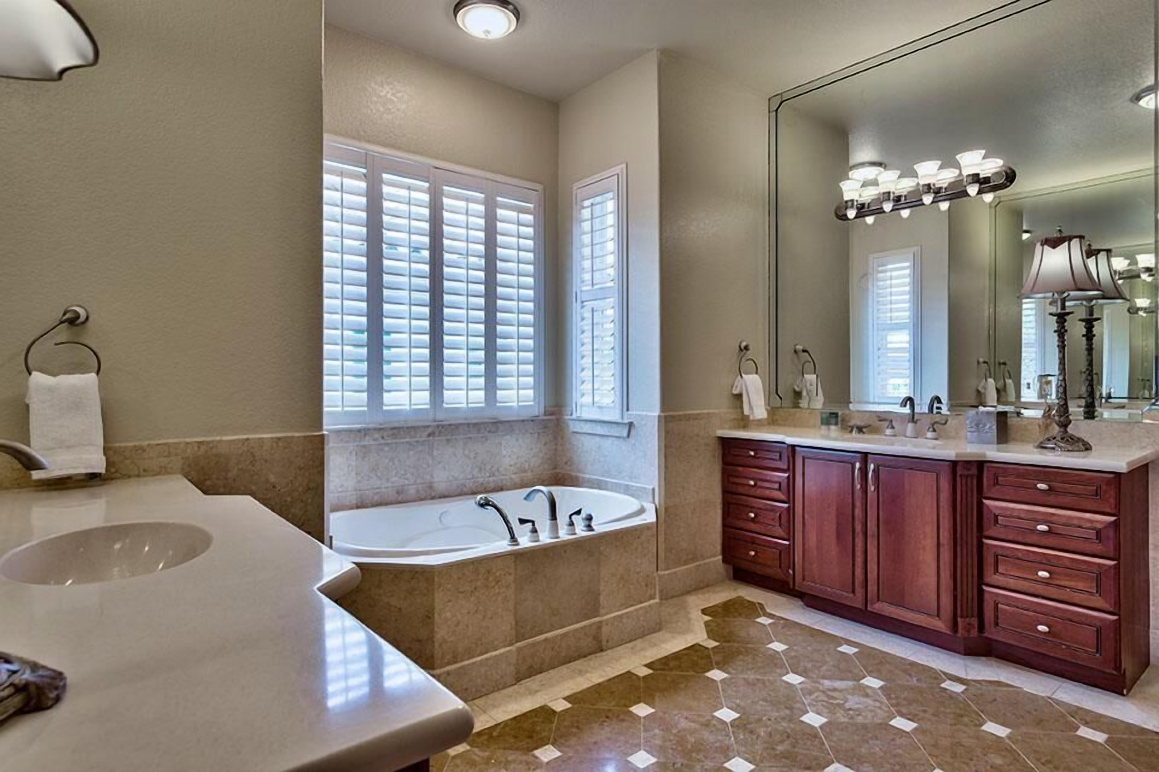 Un baño con un lavamanos grande, una bañera independiente, un tocador con espejo y un ventanal con persianas.
