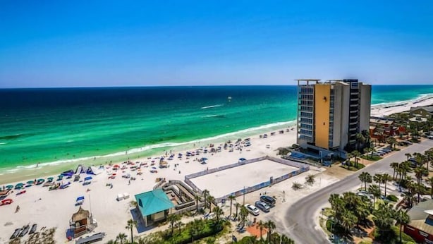 A beachside hotel with a large building, a sandy beach, and the ocean.