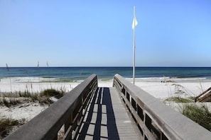 Ein hölzerner Steg führt zu einem Strand, in der Ferne weht eine Fahne.