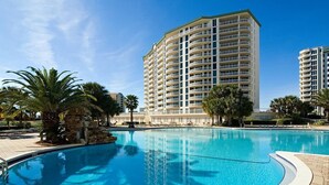 A swimming pool with a curved edge, surrounded by palm trees and a tall building in the background.