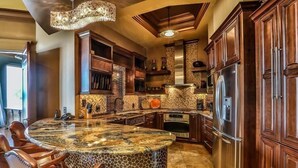A kitchen with a large island, dark wooden cabinets, and a stone backsplash.