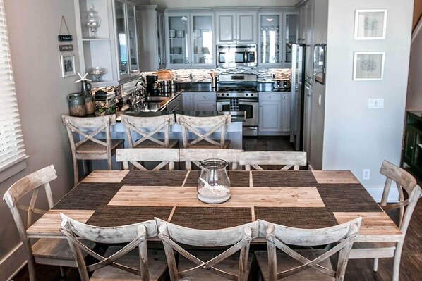 Un comedor con una mesa y sillas de madera, una cocina al fondo y una ventana con persianas.