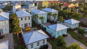 A residential area with multiple houses featuring blue roofs and white walls, surrounded by palm trees and a paved driveway. - VILLA DEL CARMEN 5 Bedroom Holiday Home by Five Star Properties (Miramar Beach)