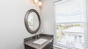 A bathroom with a granite countertop sink, a round mirror, and a window with blinds. - VILLA DEL CARMEN 5 Bedroom Holiday Home by Five Star Properties (Miramar Beach)