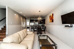 A modern living room with a sofa, a glass coffee table, and a TV mounted on the wall. - VILLA DEL CARMEN 5 Bedroom Holiday Home by Five Star Properties (Miramar Beach)