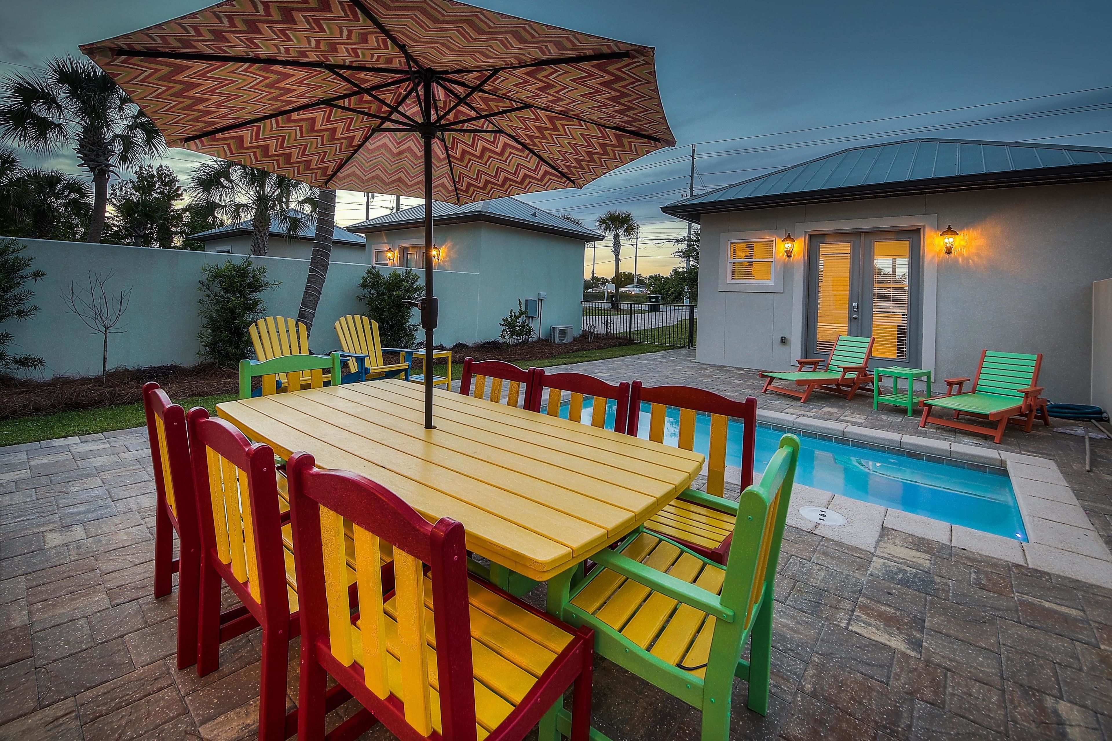 A patio area with a pool, a wooden table with chairs, and a large umbrella.