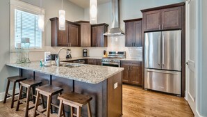 A modern kitchen with dark wood cabinets, stainless steel appliances, and a granite island with bar stools. - Villa Destiny 6 Bedroom Holiday Home by Five Star Properties (Destin)