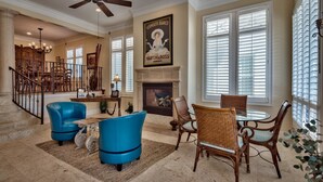 A spacious living room with a fireplace, a dining area with wicker chairs, and a staircase leading to another level.