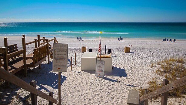 A beach with wooden benches, a lifeguard stand, and a flag.