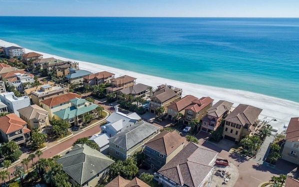 Vista aérea de una zona residencial costera con casas, una playa y un mar azul cristalino.