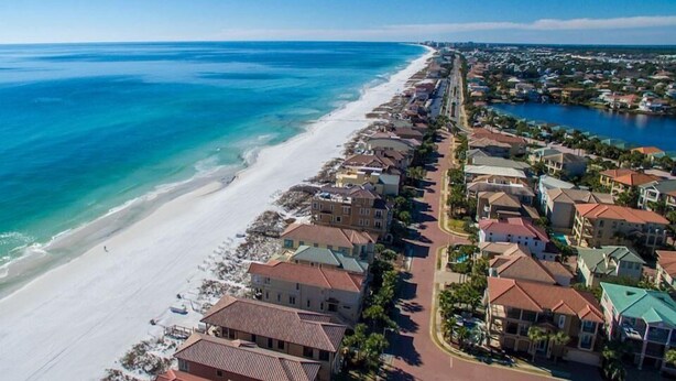 An aerial view of a coastal residential area with a beachfront, houses with red roofs, and a clear blue sky. - Honu Hale 5 Bedroom Holiday Home by Five Star Properties (Destin)