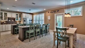A spacious kitchen with a central island, wooden flooring, and a dining area with green chairs. - Honu Hale 5 Bedroom Holiday Home by Five Star Properties (Destin)