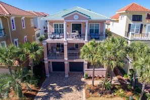 A multi-story residential building with a balcony, palm trees, and a clear sky.