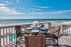 Una mesa de comedor con cuatro sillas de mimbre en una terraza de madera con vistas al océano.