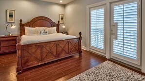 Un dormitorio con cama de madera, dos lámparas de noche, ventilador de techo y un ventanal con persianas.