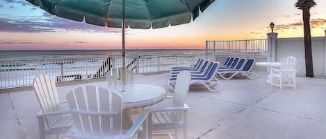 A patio with white Adirondack chairs, a round table, and a green umbrella.