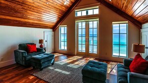 A spacious loft with wooden ceiling beams, large windows with ocean views, and a cozy seating area with plush sofas and a patterned rug. - Kates Porch 7 Bedroom Holiday Home by Five Star Properties (Miramar Beach)