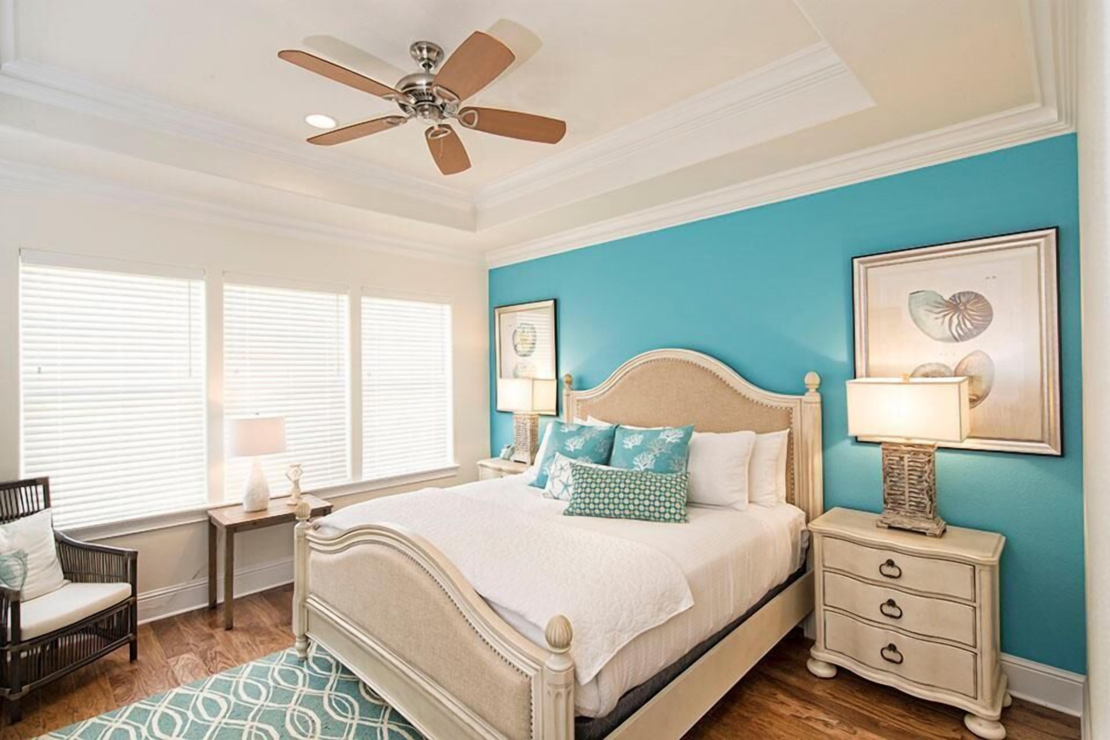 A bedroom with a bed, a nightstand, a chair, a ceiling fan, and a window with blinds.