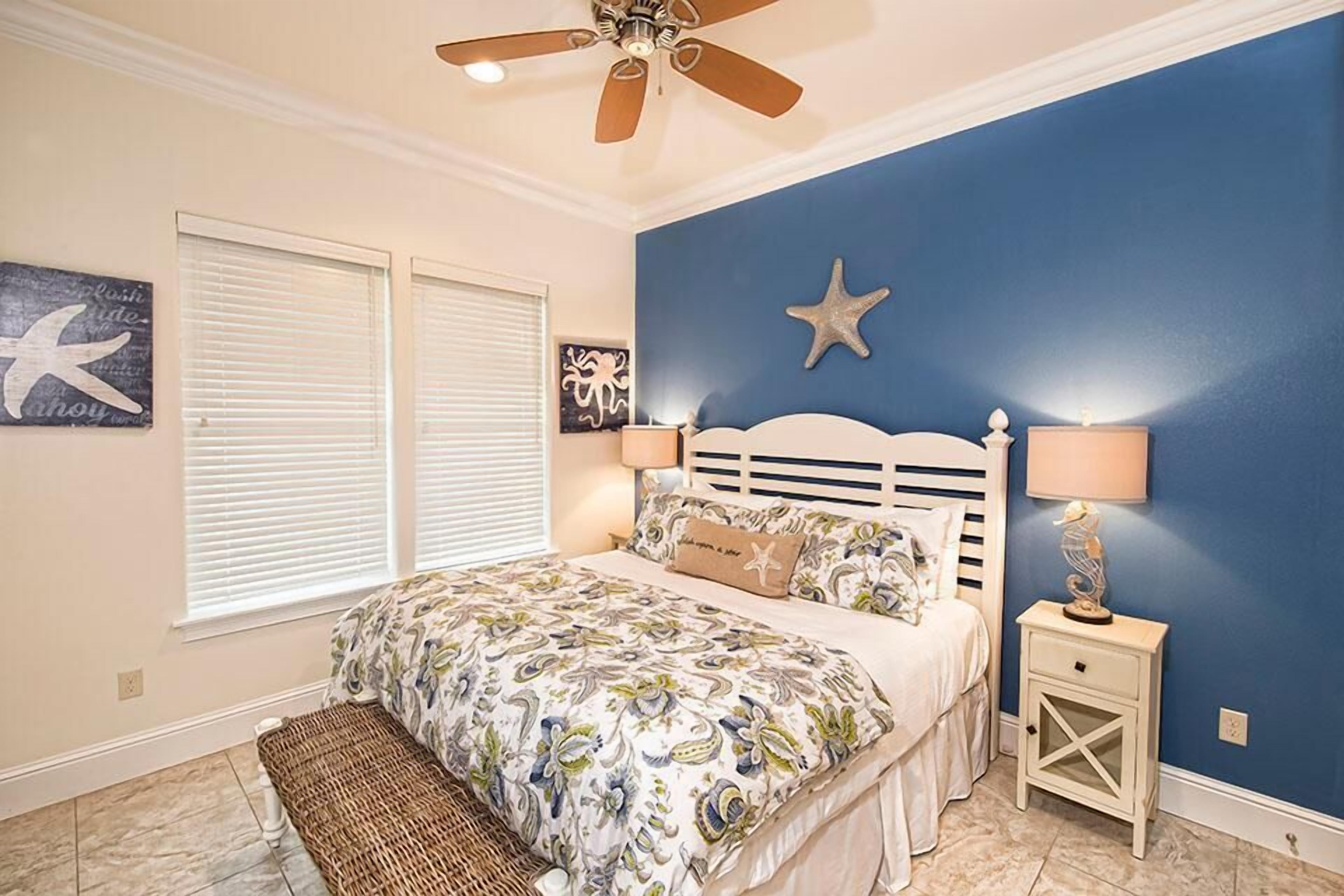 Quarto com cama, ventoinha no teto, decoração com estrela-do-mar e mesa de cabeceira com abajur.