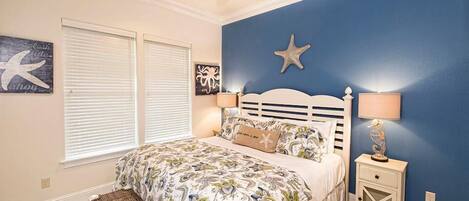 Quarto com cama, ventoinha no teto, decoração com estrela-do-mar e mesa de cabeceira com abajur.