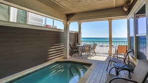 A covered outdoor area with a pool, wooden deck, and a view of the ocean.