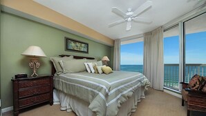 Ein Schlafzimmer mit Bett, Nachttisch, Kommode, Deckenventilator und einem großen Fenster mit Meerblick.