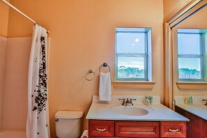 Un baño con inodoro, lavamanos y cortina de ducha. Hay una ventana sobre el lavamanos y una toalla colgada en la pared.