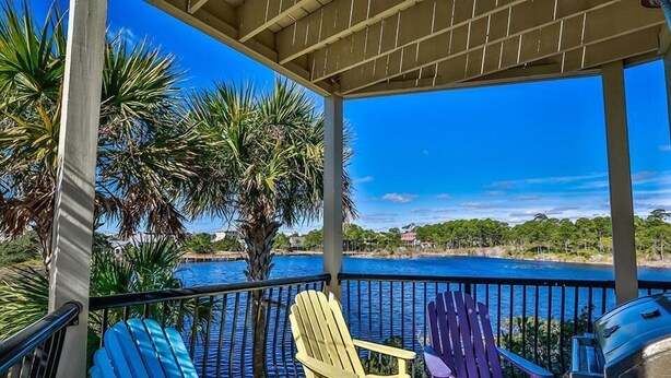 Un espacio al aire libre cubierto con vista al agua, con sillas Adirondack de colores y una parrilla.