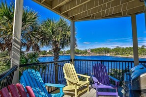 Un espacio al aire libre cubierto con vista al agua, con sillas Adirondack de colores y una parrilla.