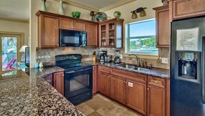 Una cocina con encimeras de granito, armarios de madera, estufa negra, microondas y refrigerador.