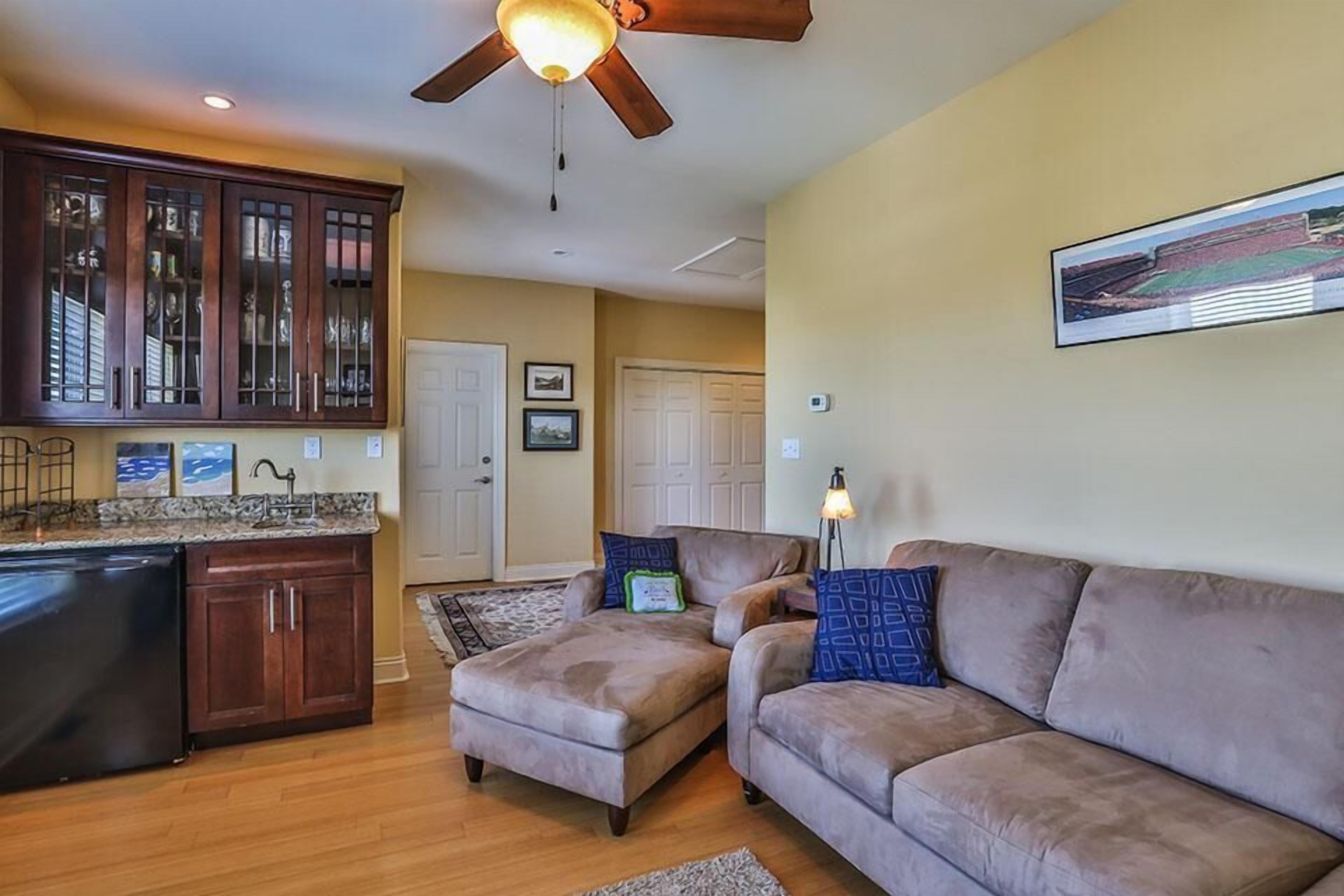 A living room with a brown sofa, a kitchen with wooden cabinets, and a ceiling fan.