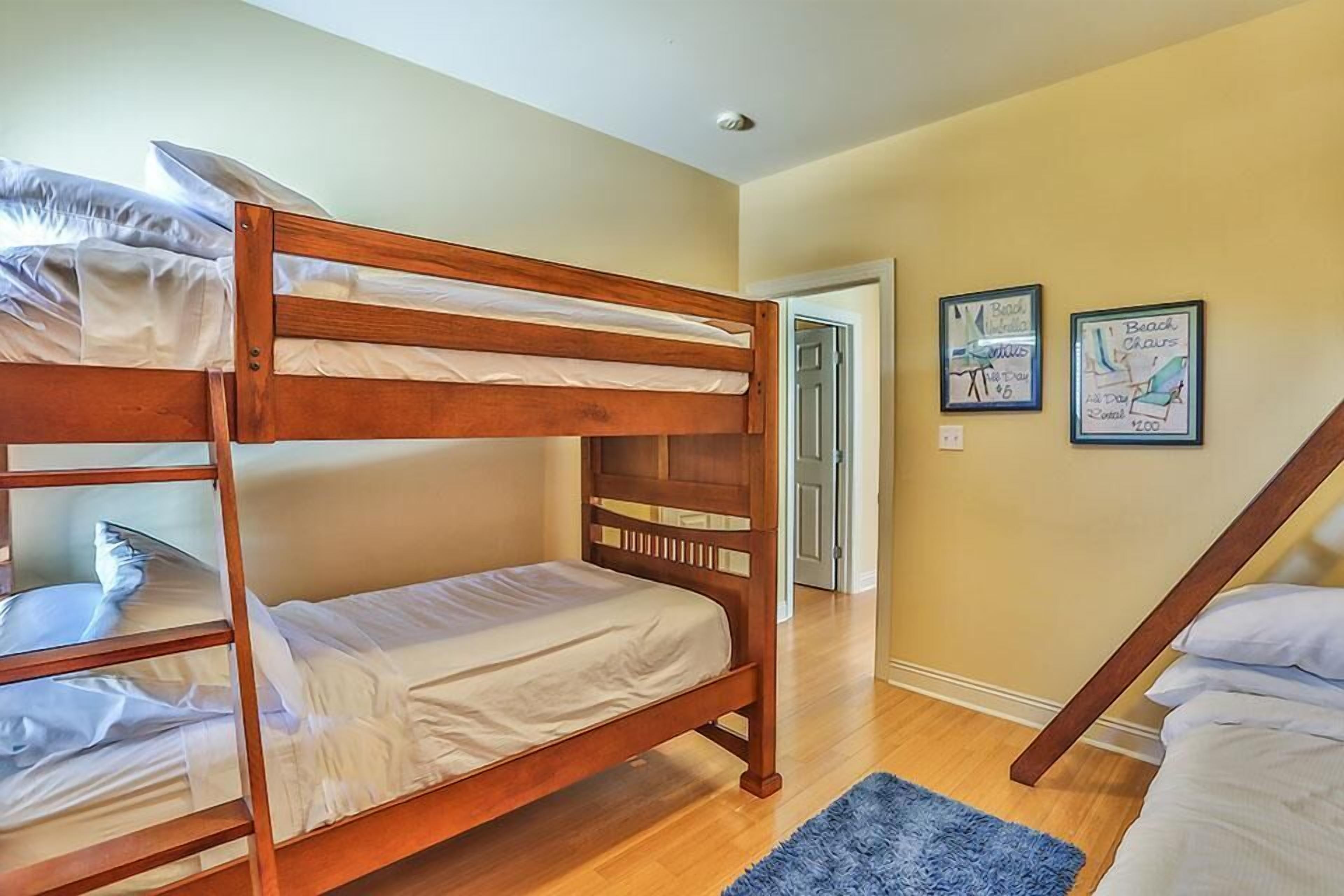 A bunk bed room with wooden frames, a blue rug, and two framed pictures on the wall.