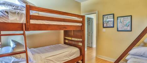 A bunk bed room with wooden frames, a blue rug, and two framed pictures on the wall.