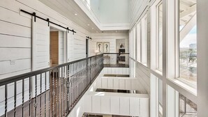A multi-level interior with a central staircase, white paneled walls, and large windows. - Looking Glass 5 Bedroom Holiday Home by Five Star Properties (Santa Rosa Beach)