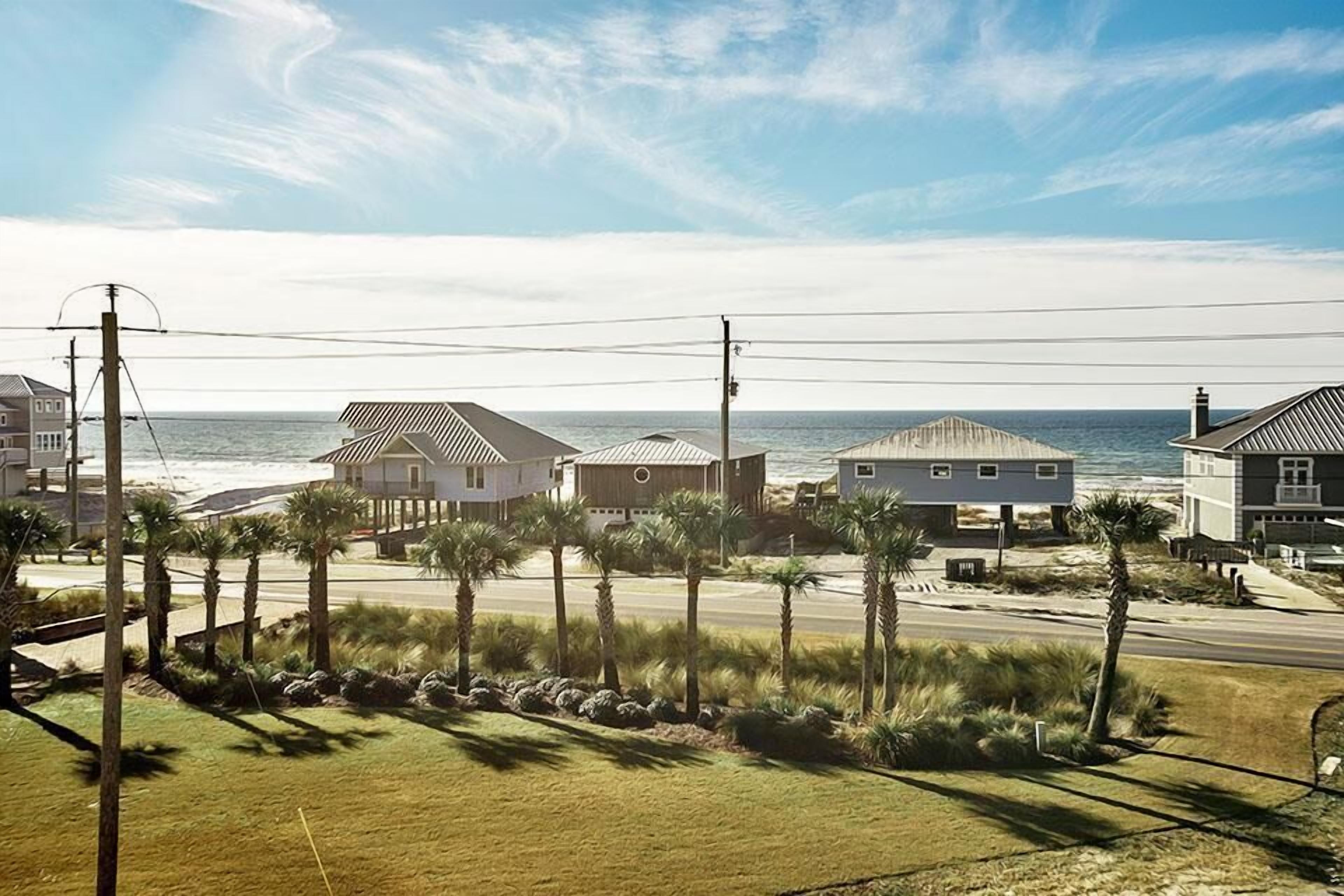 A coastal residential area with houses, a road, and a beach in the background.