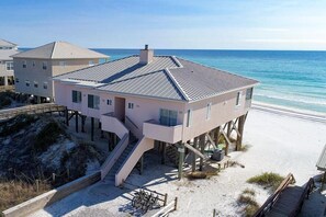 Een strandhuis met een overdekt terras, een trap naar het strand en uitzicht op de oceaan.