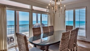 A dining area with a glass table surrounded by wicker chairs, large windows with ocean views, and a chandelier. - Luna Sea 4 Bedroom Holiday Home by Five Star Properties (Santa Rosa Beach)